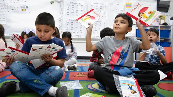 Students sit on the floor of a classroom holding books