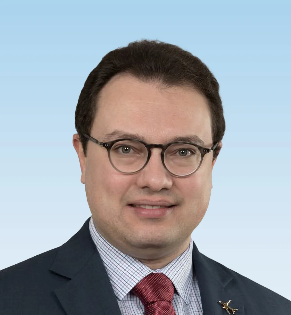 A headshot of Gale Le Bris, a man with dark hair and glasses wearing a black suit jacket, red tie and blue check shirt.