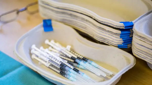 A handful of syringes containing COVID-19 vaccine doses rest in a cardboard tray.