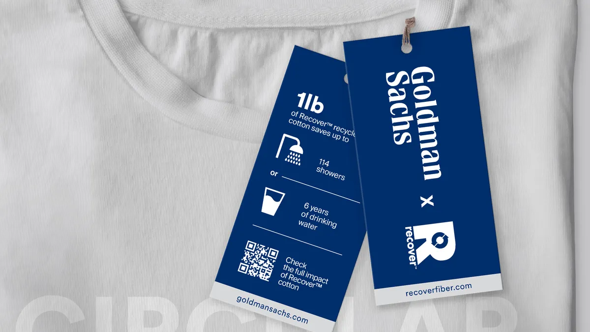 White T-shirt with a Recover and Goldman Sachs blue tag.