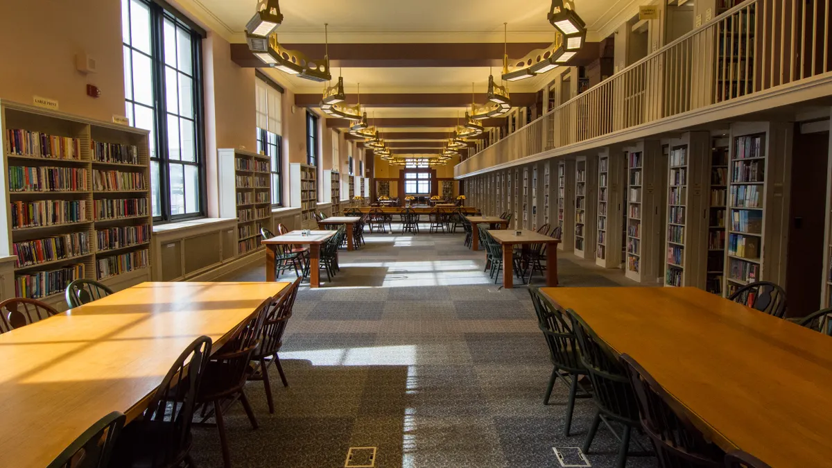 Large room with windows on one side and stacks of books on another and a long table with several chairs along the window wall.