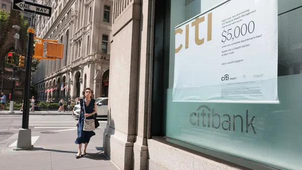 A person walks past a stone storefront that shows a promotional poster in the window.