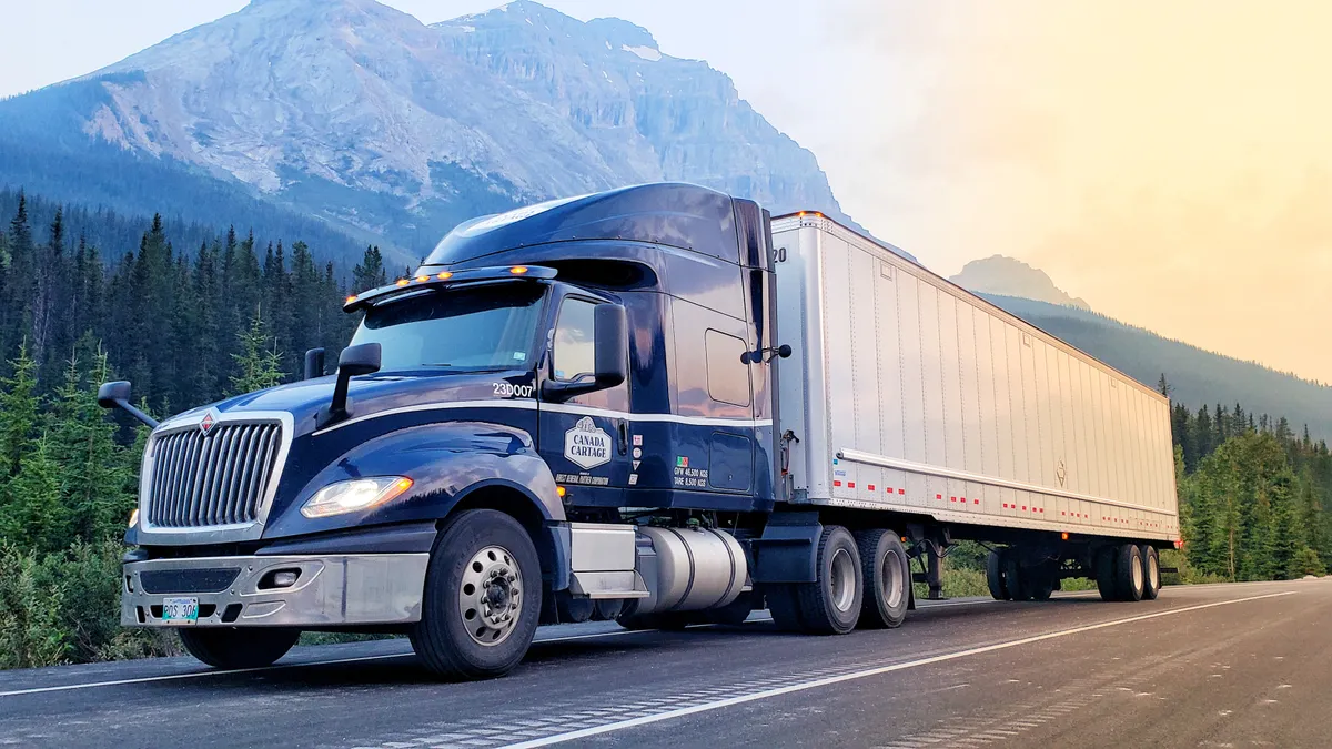 A Canada Cartage tractor-trailer on a road with mountains in the background.