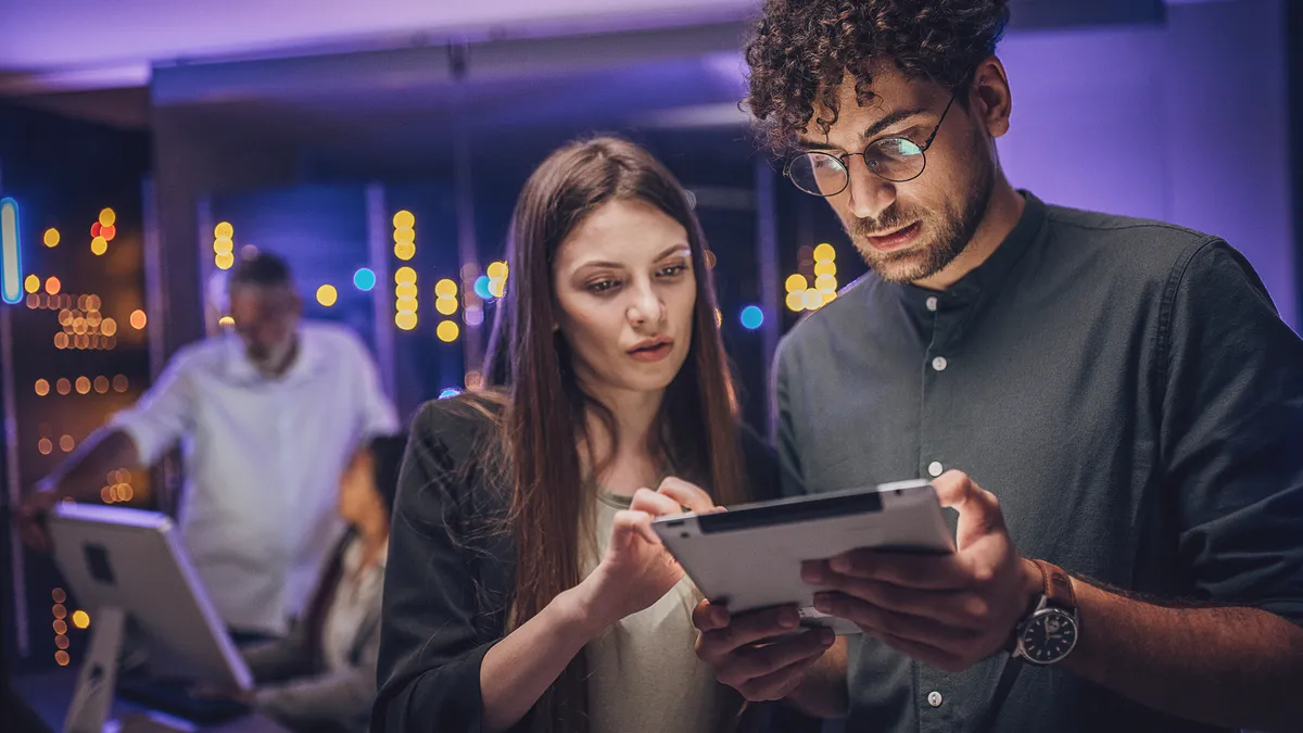 Male and female maintenance engineers examining data on digital tablet in a server room.