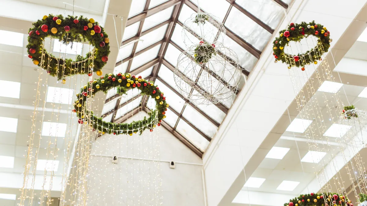 View of an interior of a mall decorated with holiday wreaths attached to the skylight.