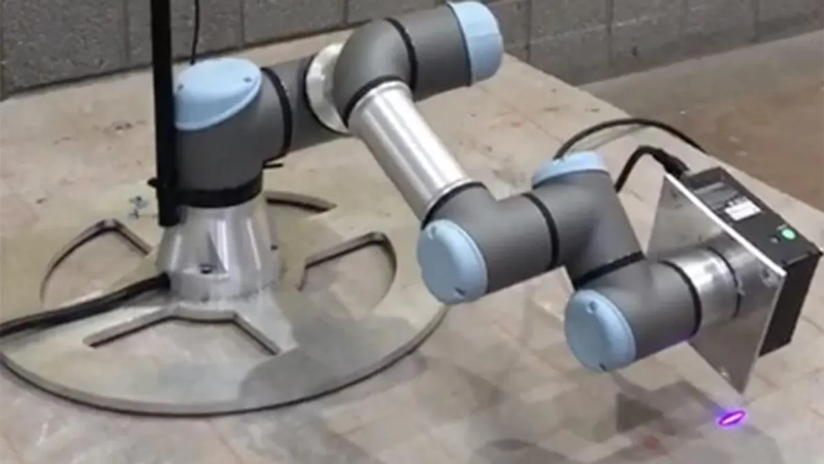 A robot sits on a bed of concrete. It's sleek and off-white, with a visual lens on the front.