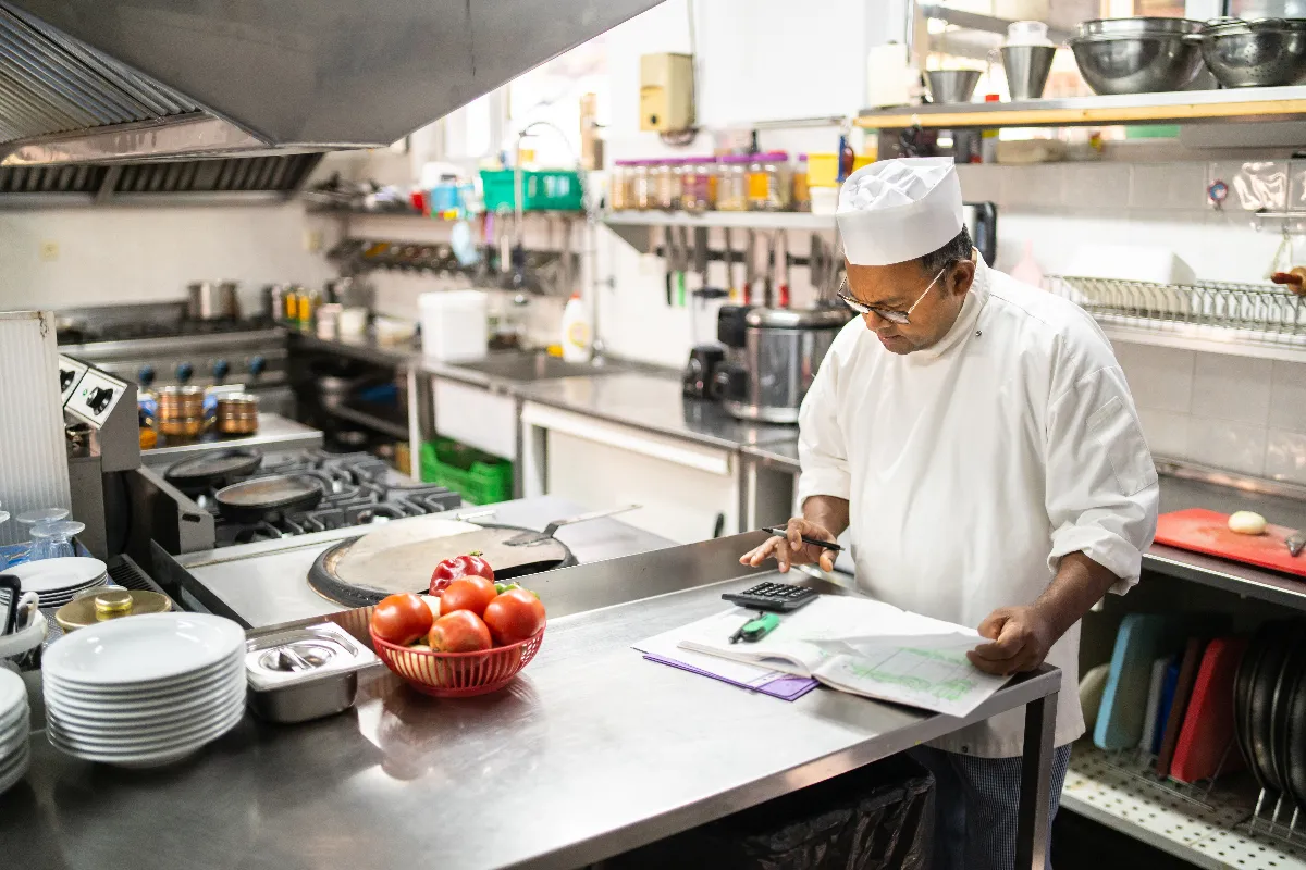 A picture of a chef in a kitchen looking down at a calculator.