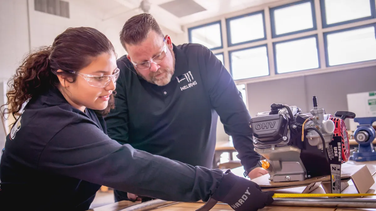 A female high school student measures an engine while her instructor Brent Tuttle supervises as part of the LA County Skilled Trades Summers program.