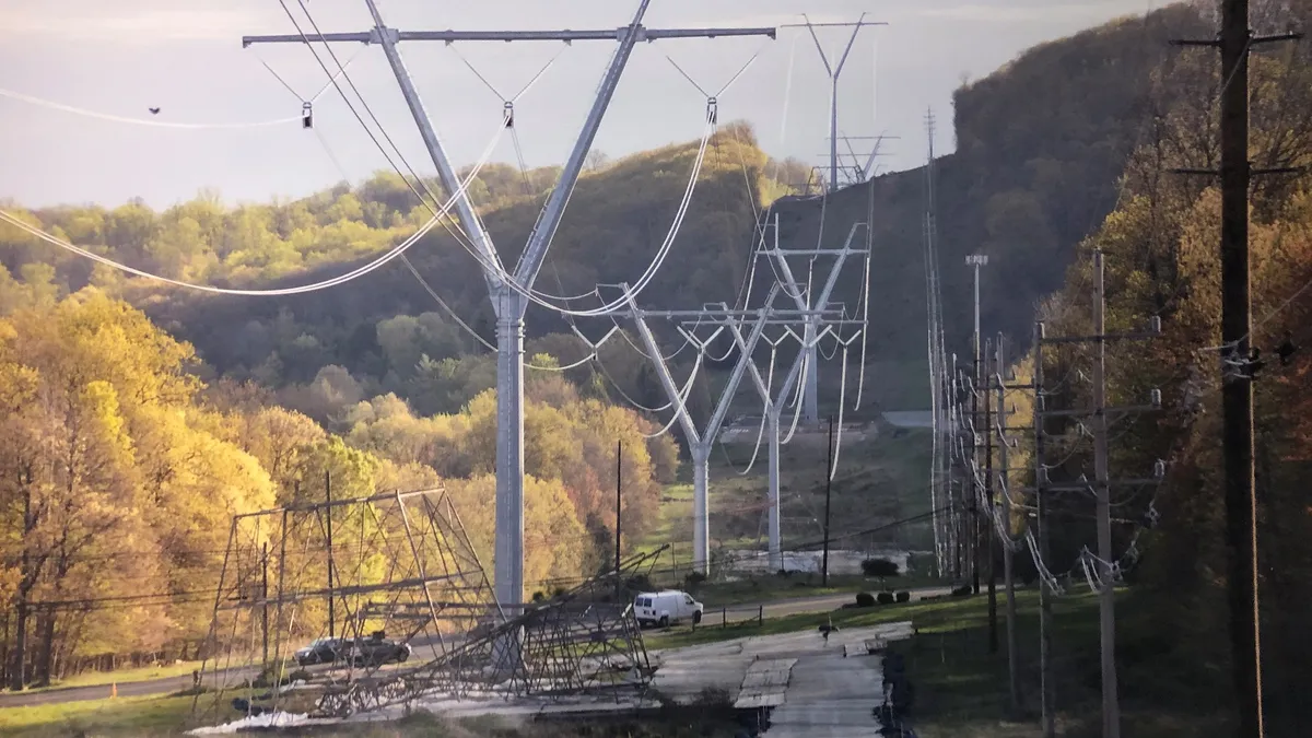 Electric transmission lines run up a hill through a wooded area.