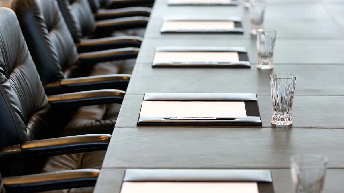 Close-up of water glasses and portfolios on a long desk with a row of empty chairs.