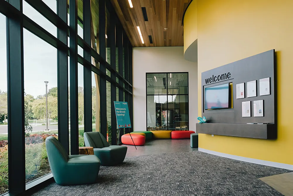 A lobby of a building is shown, with green chairs to the left and a "Welcome" sign to the right.