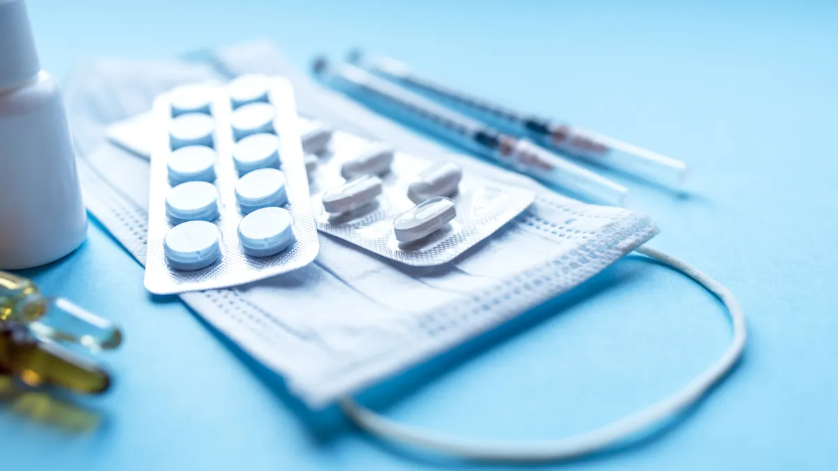 Two packets of pills and a vaccine vials sit atop a blue surgical mask.