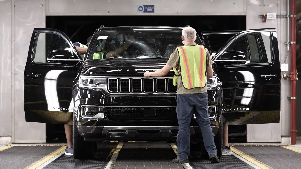 Employees wearing safety vests at the Warren Truck Assembly Plant inspect a black Jeep Wagoneer after it emerges from the water test booth.