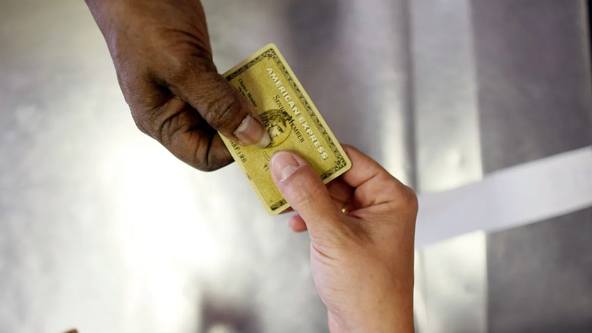 A gold American Express card being passed between two hands