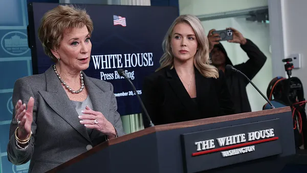 Linda McMahon speaks at a podium during a press conference while Karoline Leavitt, by her side, watches.