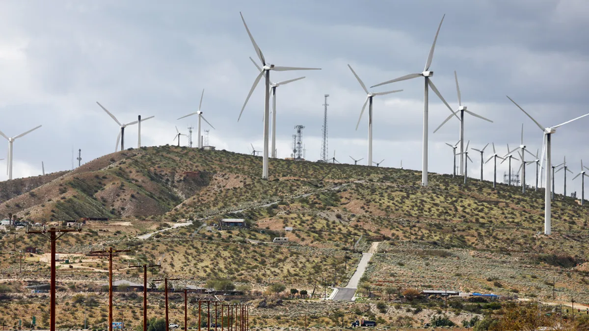 Wind turbines operate at a wind farm in Coachella Valley, as vehicles drive on a highway below.