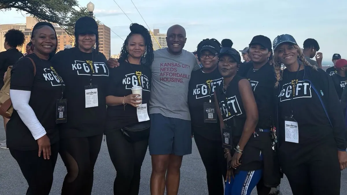 A person wearing a t-shirt that says "Build Affordable Housing" standing with group of people wearing black pants and black t-shirts.