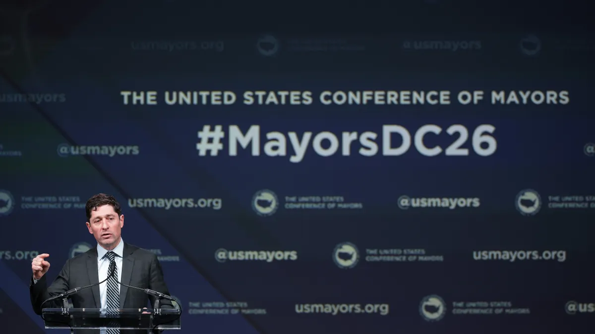 Person at a podium in front of sign that says "U.S. Conference of Mayors DC26"