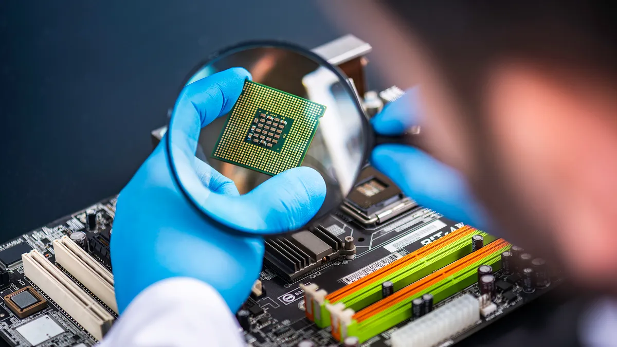 A person wearing blue latex gloves holding a magnifying glass over a microchip.