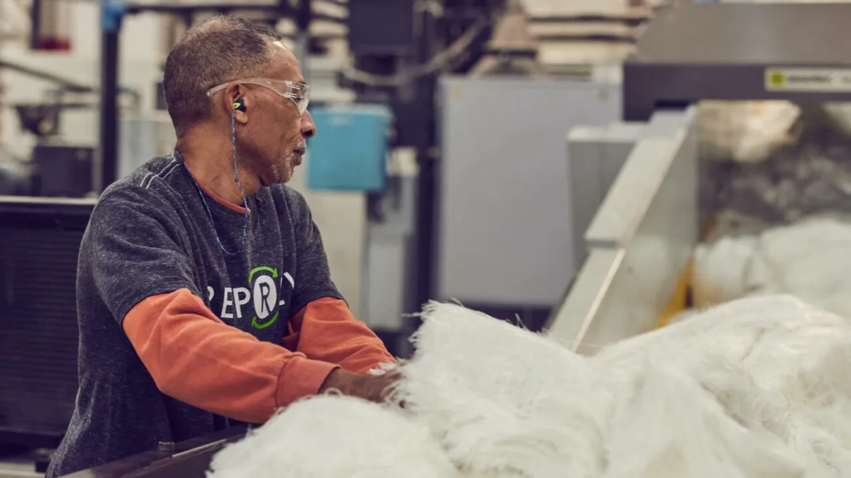 A person works in a Repreve factory, watching over yarn and fiber in a machine.