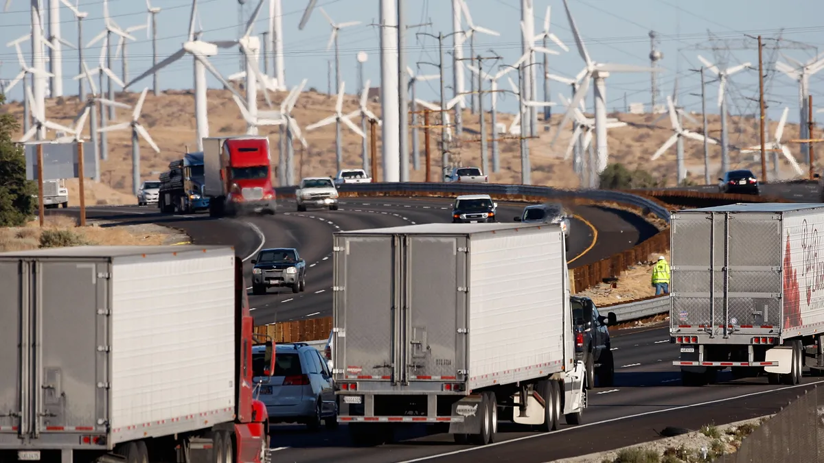 Transport trucks and cars drive down a highway with windmills in the background