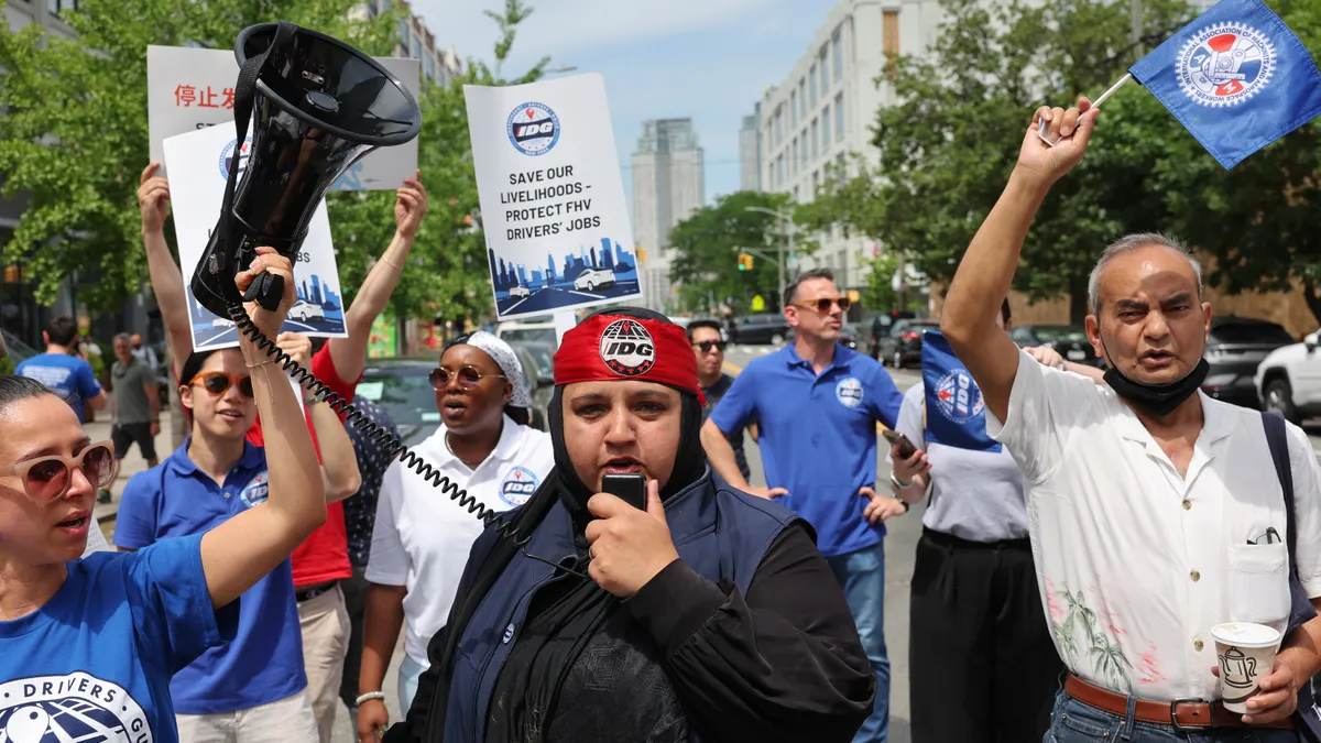 A man with a bullhorn surrounded by a group of men and women, some holding flags and protest signs.