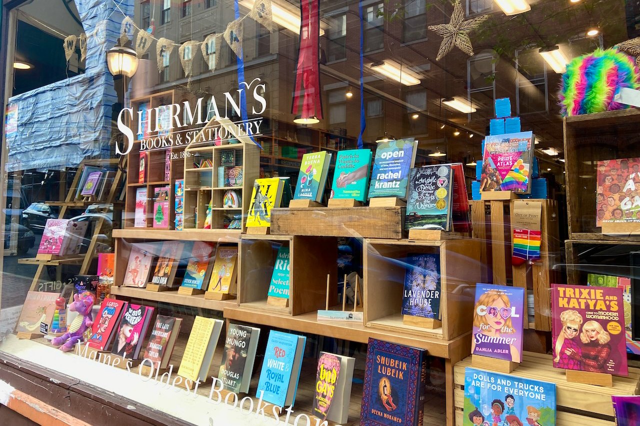 The window of bookstore featuring Pride-themed decorations and books for all ages.