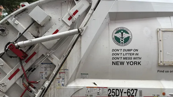 The exterior of a rear-loading garbage truck with the New York City Sanitation Department's logo emblazoned on the side.