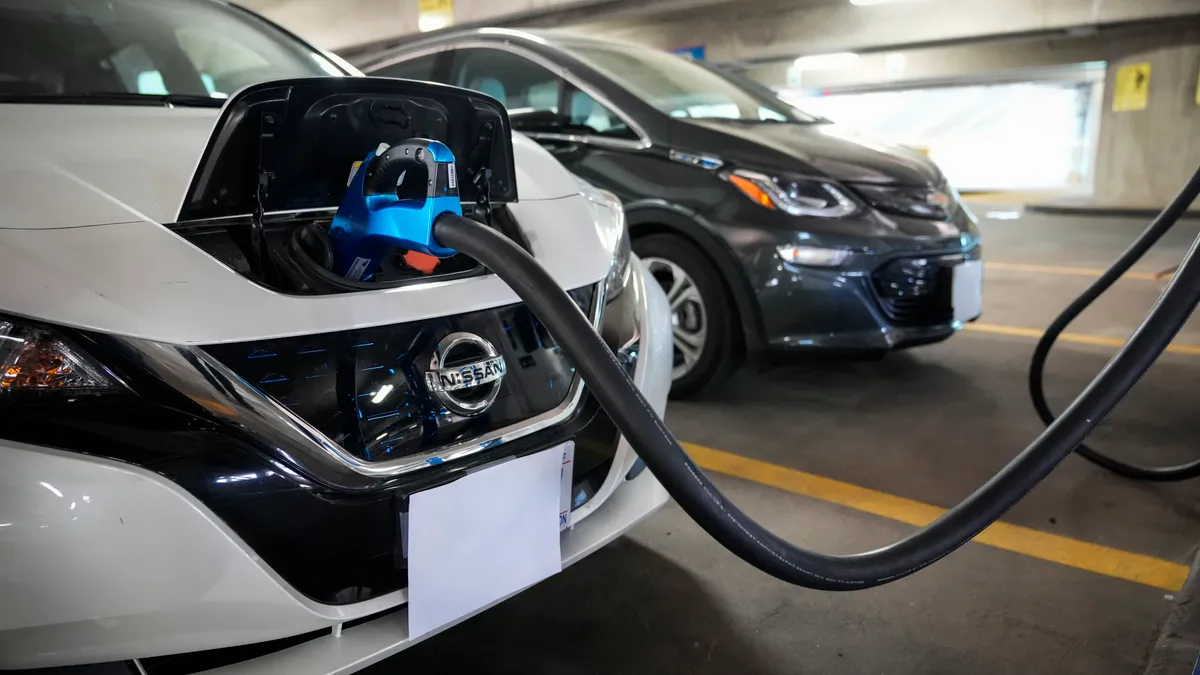 Two vehicles parked in a garage, with an electric charging cable connceted to a white Nissan in the foreground.