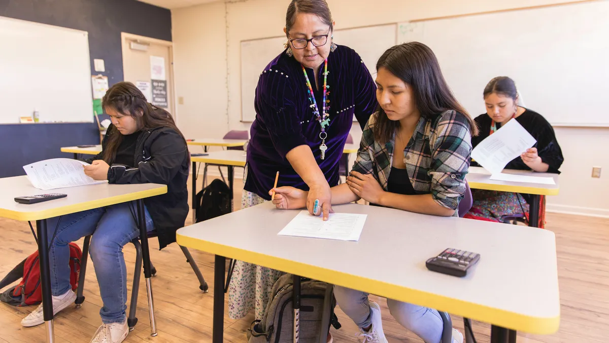 A teacher points to a paper on the desk of a high school student