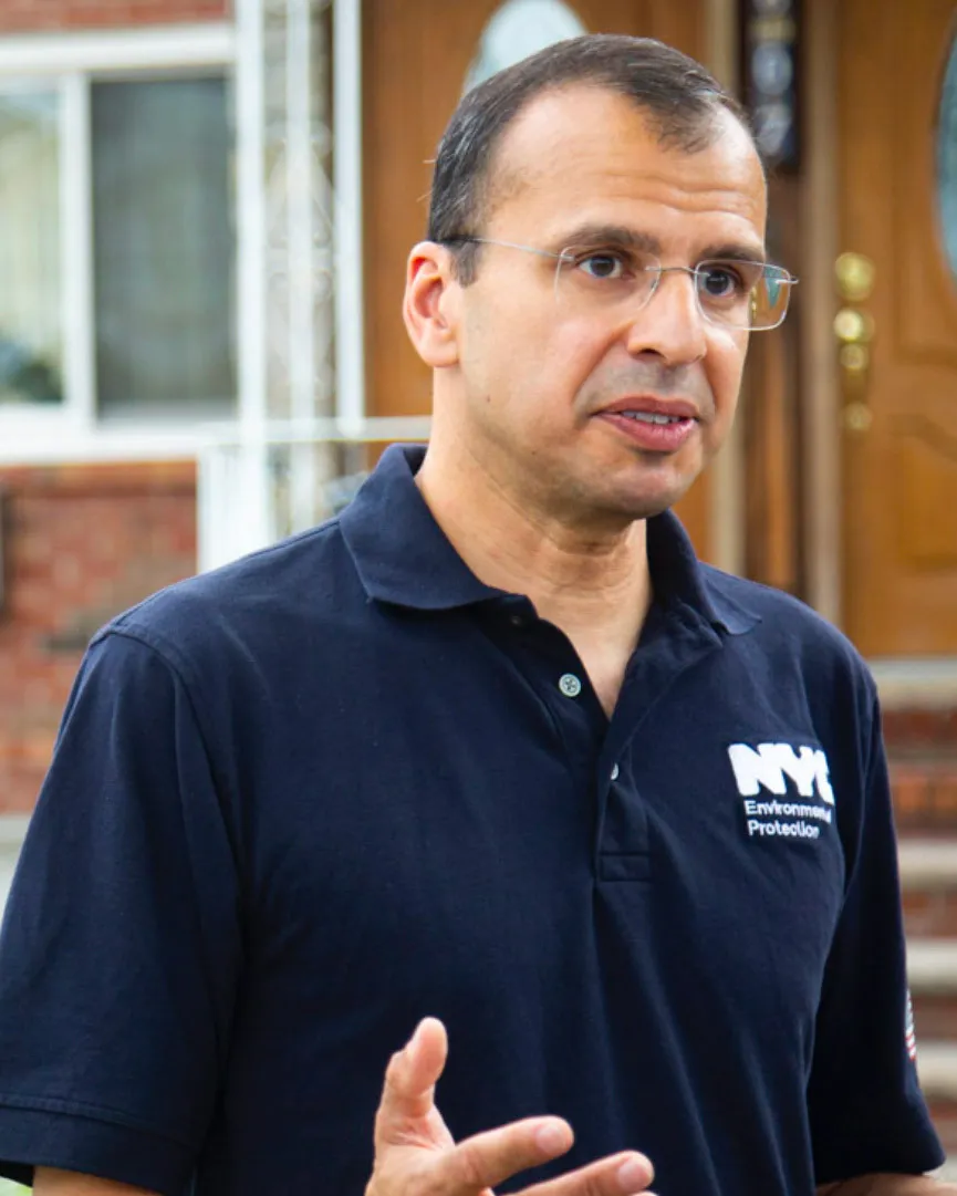 A person in glasses speaks in front of a home.