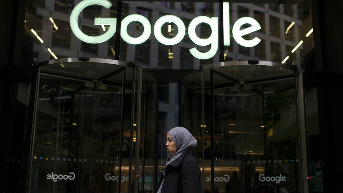 A woman walks past the front of a glass building with the Google logo.