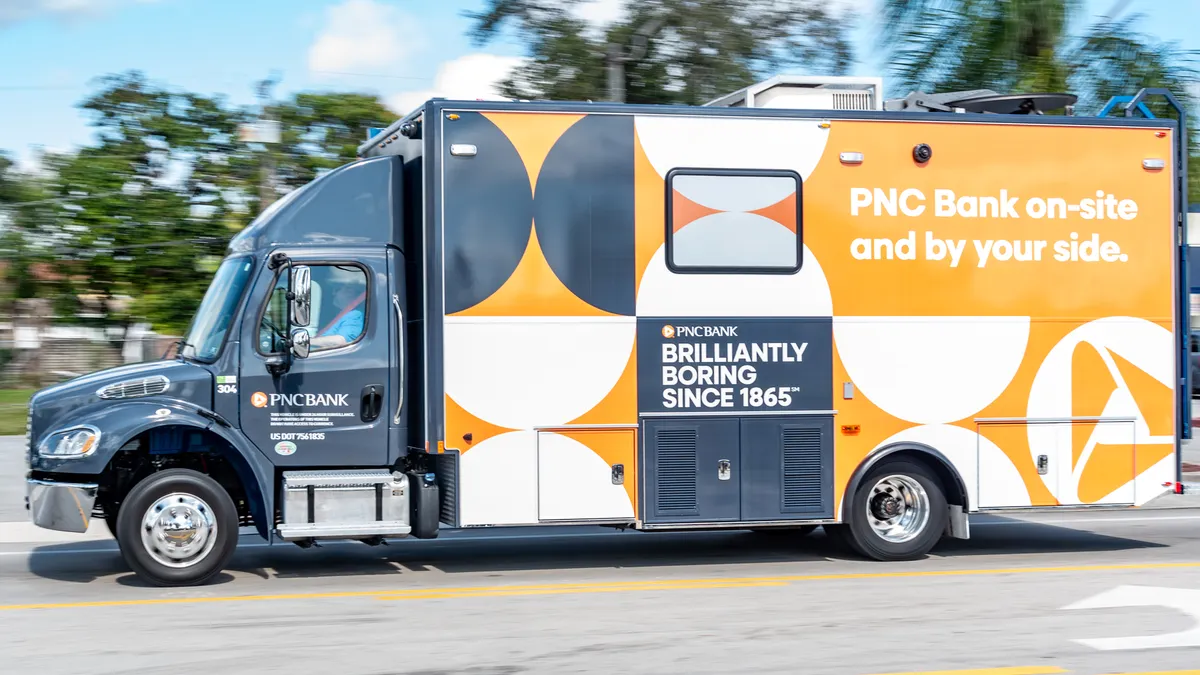 A commercial vehicle that operates as a mobile bank branch, with PNC signage and branding, drives down a street.