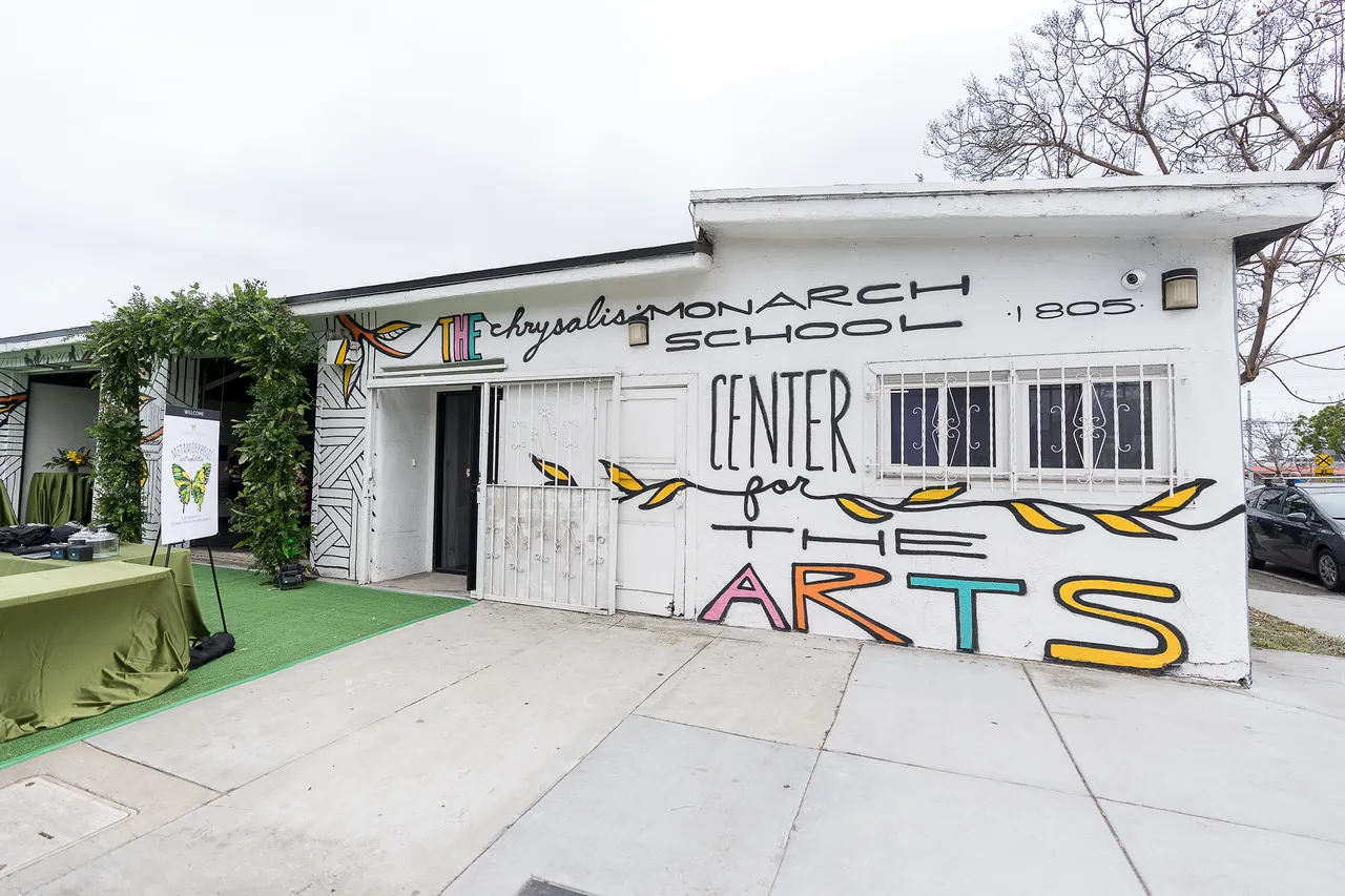 A white, one-story building that serves as a high school's arts center is shown adorned in brightly colored paint identifying it as the Monarch School's Center for the Arts.