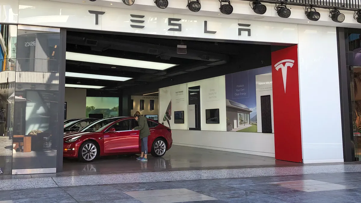 Looking into a Tesla showroom, a person opens the door of a red car and looks inside.