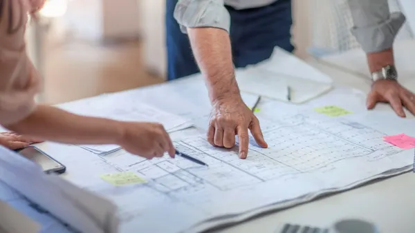 A view of construction plans, with two people pointing at the drawings.