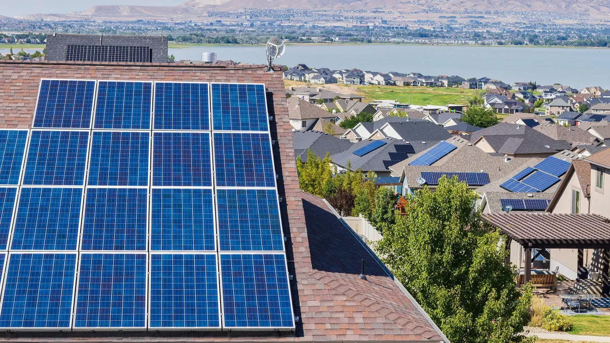 Rooftop solar panels installed on a suburban home, with a neighborhood full of houses and mountains in the background under a sunny sky.
