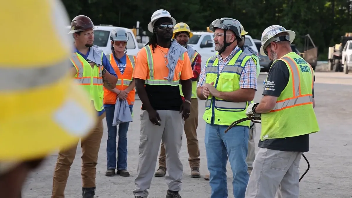 A group of people stand around a jobsite having a conversation.