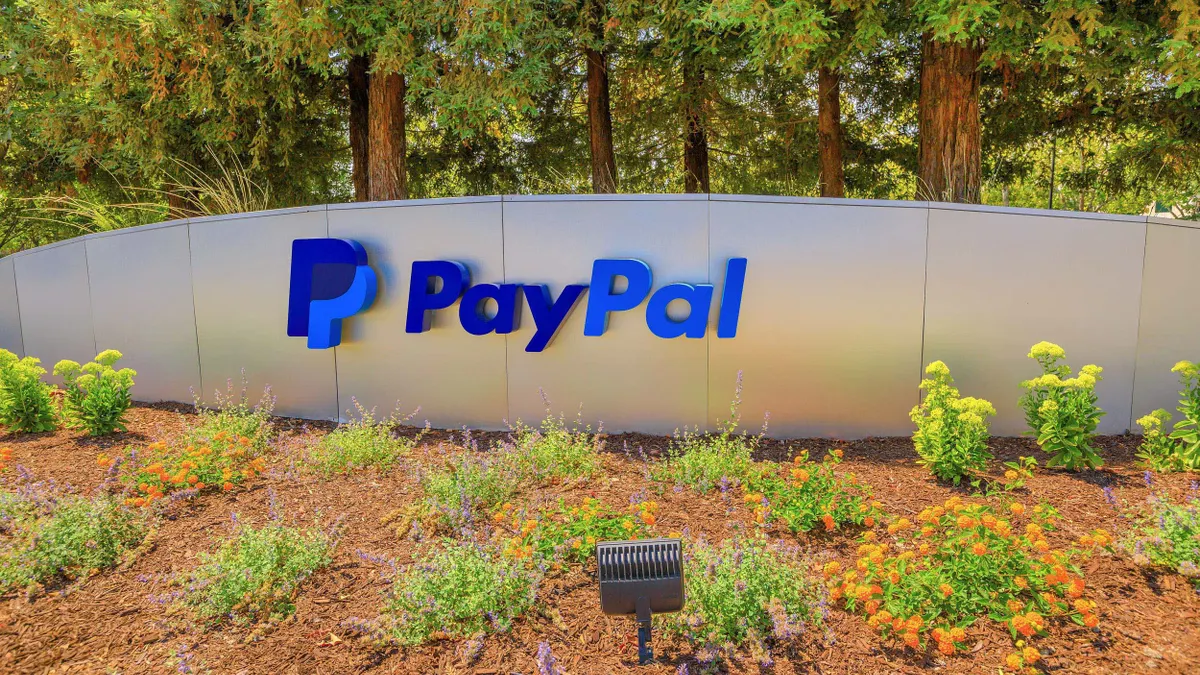 A Paypal logo and sign is mounted to a metal entrance monument surrounded by shrugs and trees. 