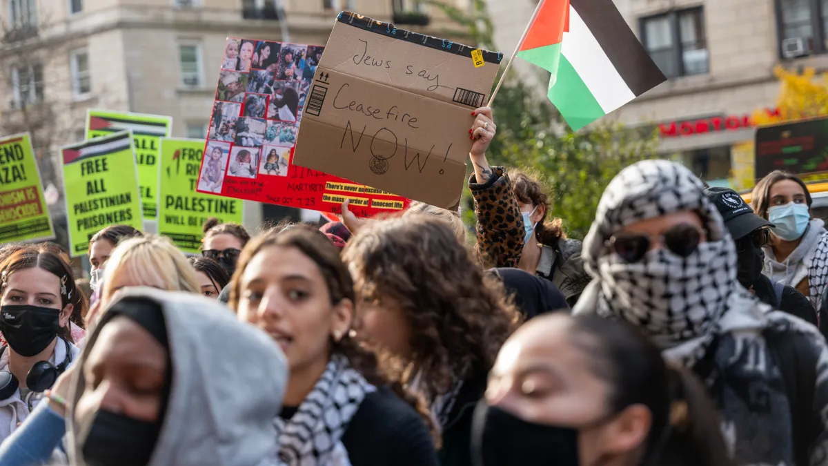 A crowd photo of students carrying protest signs and the Palestine flag. One prominent sign reads "Jews say ceasefire now!"