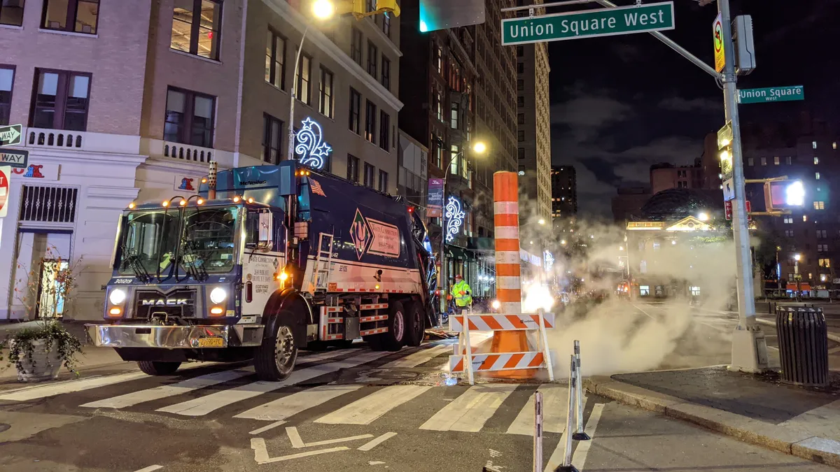 A Waste Connections truck drives down a New York street at night, with a Union Square West sign overhead