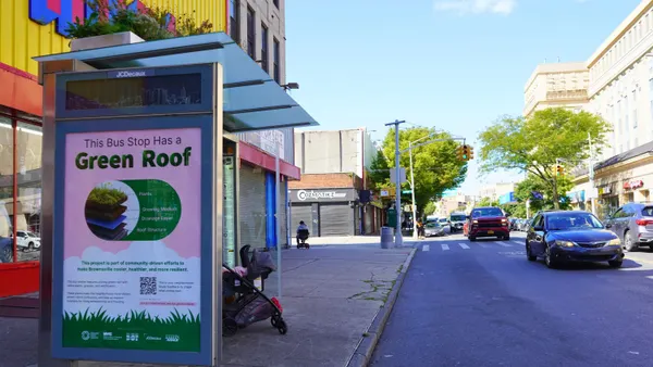 A bus shelter with plants on the roof on a street with cars going by.