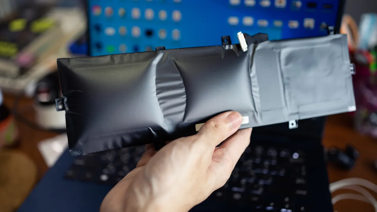 A hand holds a damaged laptop battery