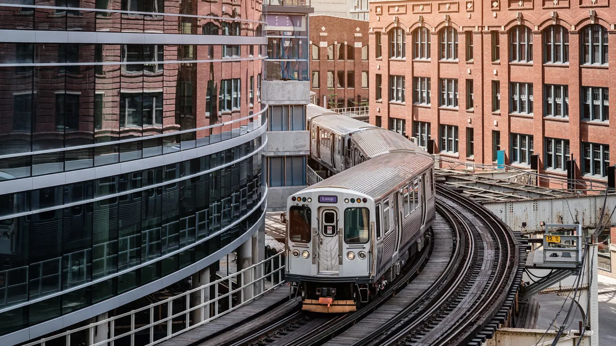 Chicago silver colored commuter train moving on elevated tracks to railroad station in between urban city buildings of Chicago, Illinois.