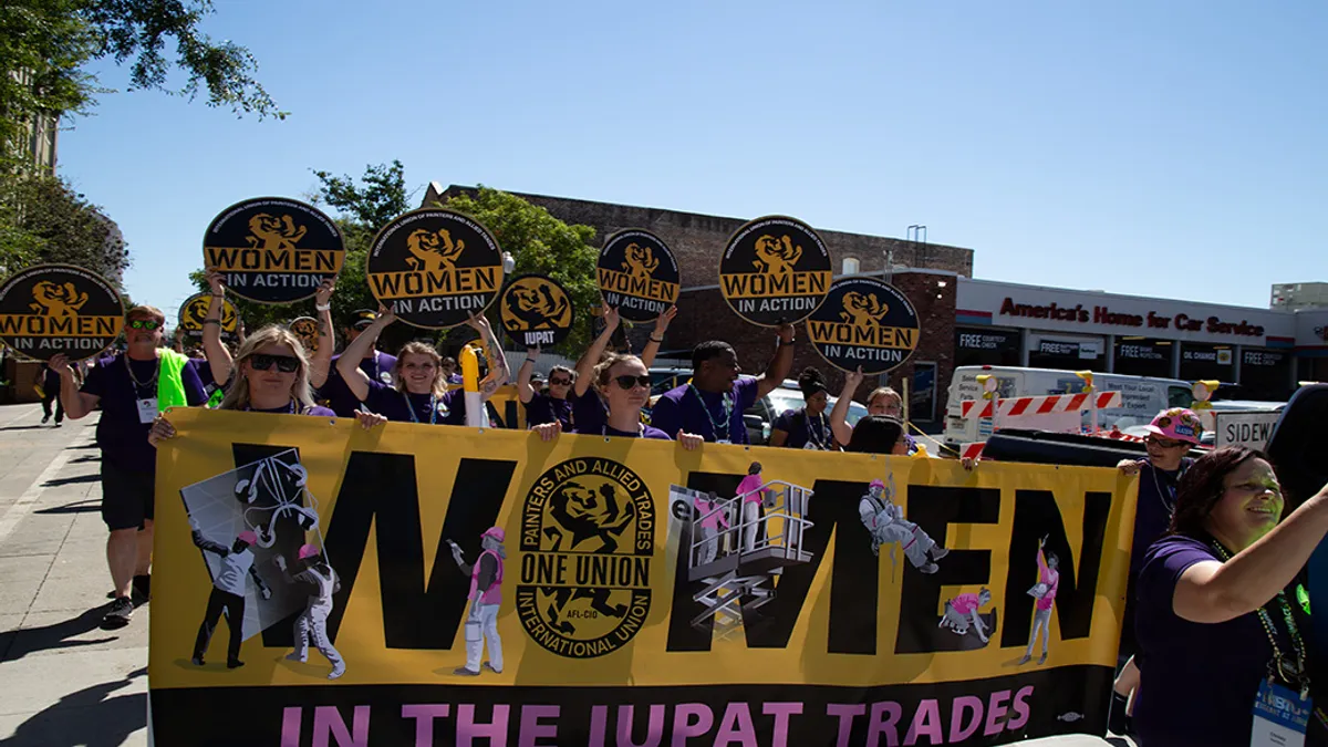 Group of people holding a 'Women in the IUPAT Trades' banner at an event.