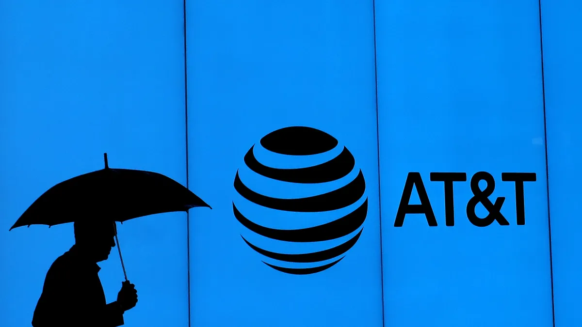 A man walks with an umbrella in front of AT&T logo.