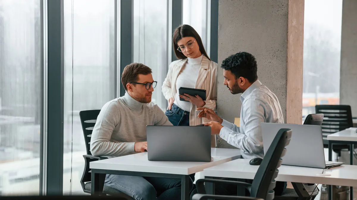 Three people talking at a desk with a laptop.