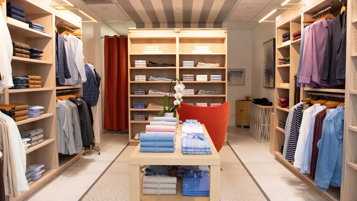 Folded business shirts and other merchandise sit on blond wood shelves.