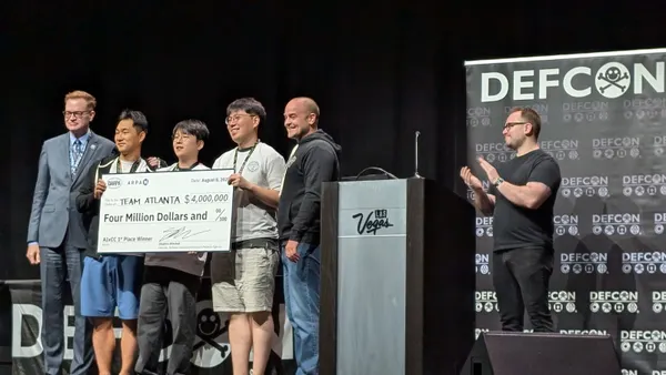 Six men stand on a stage. Three men hold an oversized $4 million check made out to "Team Atlanta," while two of the other men flank this trio and pose for a photo with them. The sixth person stands off to the side and applauds.
