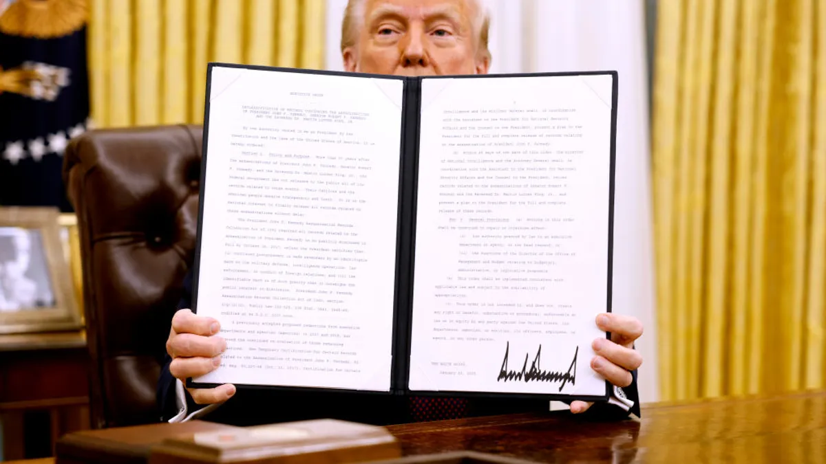 President Donald Trump's top portion of his face can be seen behind an open folder he is holding. His is in the Oval Office and seated as a desk.